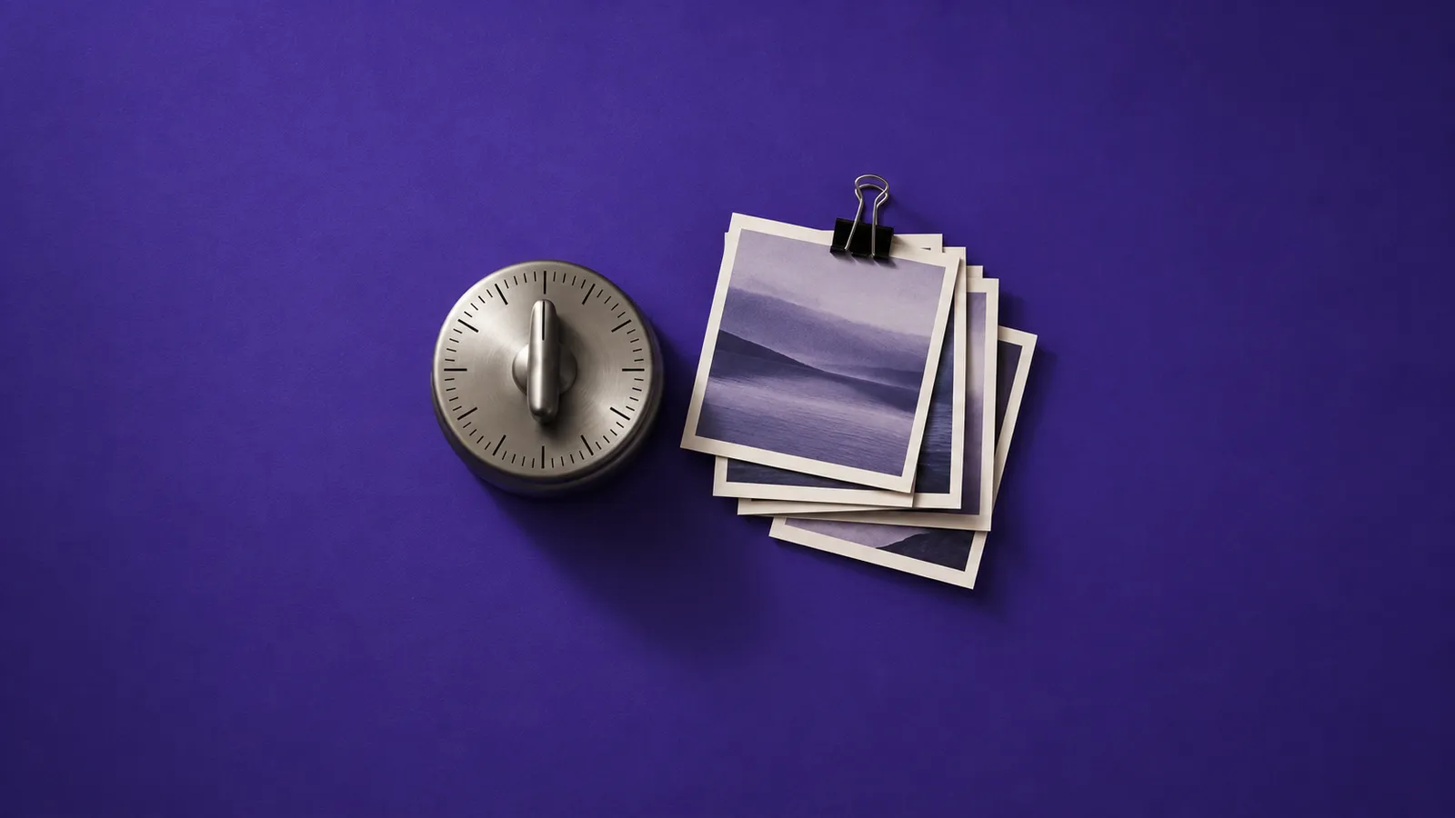 Timer de cozinha de metal ao lado de uma pilha de fotos quadradas presas por um clipe, sobre papel violeta