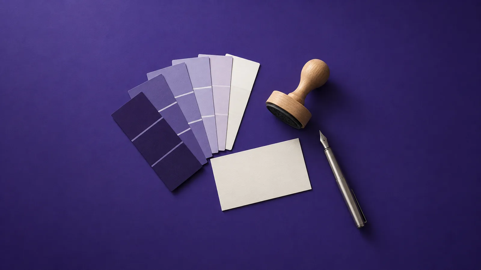 Leque de amostras de cor do violeta ao branco, um cartão em branco, um carimbo de madeira e uma caneta-tinteiro, sobre papel violeta