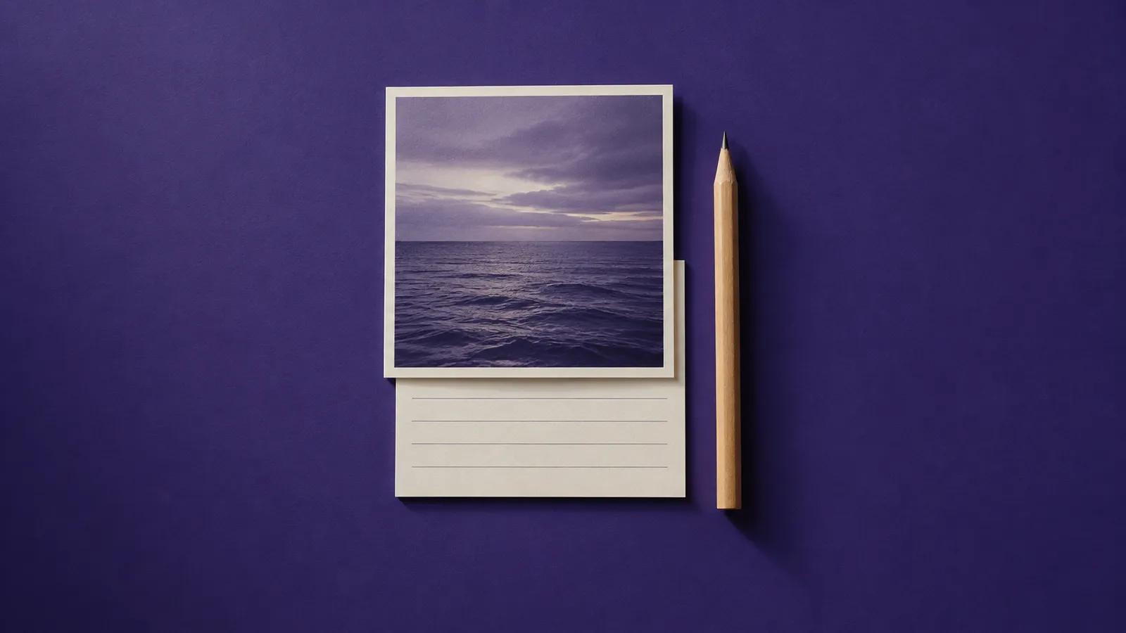 Foto quadrada do mar sobre uma ficha pautada ainda em branco, com um lápis ao lado, sobre papel violeta