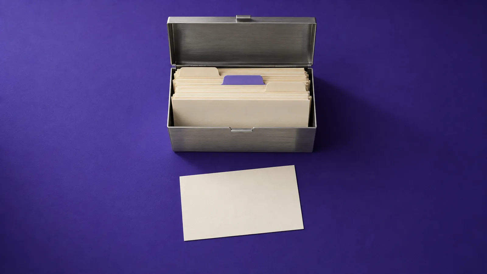 Fichário de metal aberto, cheio de fichas com divisórias, e uma ficha em branco à frente, sobre papel violeta